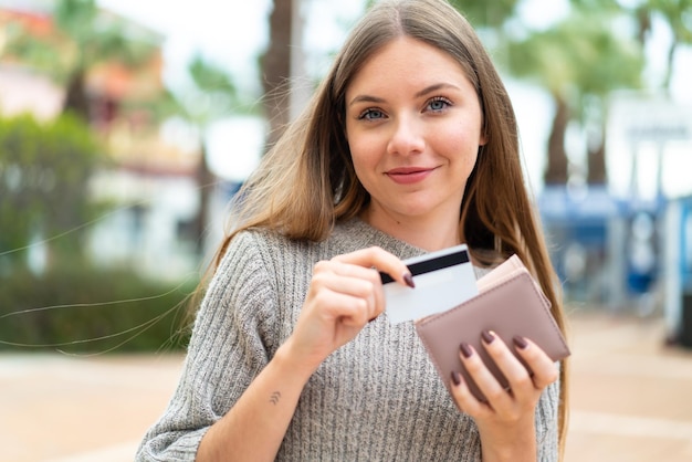 Young pretty blonde woman holding wallet and credit card with happy expression