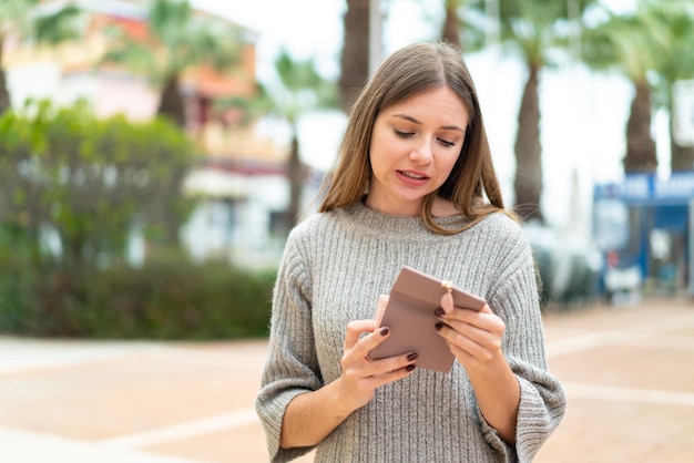 Young pretty blonde woman holding a wallet and with sad expression