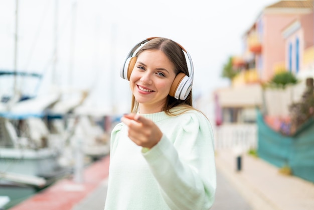 Young pretty blonde woman listening music and pointing to the front