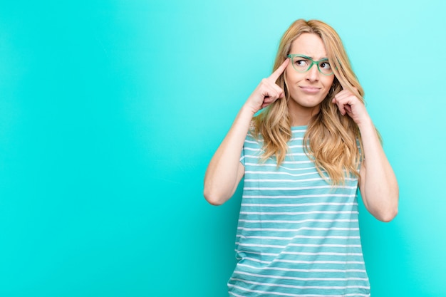 Giovane donna bionda graziosa che sembra concentrata e che pensa intensamente a un'idea, immaginando una soluzione a una sfida o un problema sopra la parete di colore