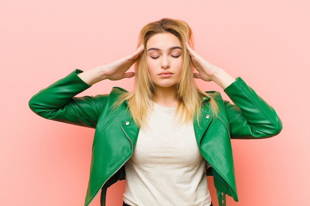 Young pretty blonde woman looking concentrated, thoughtful and inspired, brainstorming and imagining with hands on forehead over pink wall