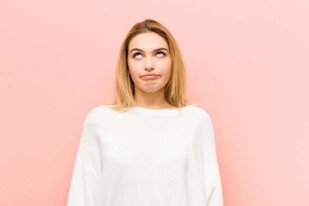 Young pretty blonde woman looking goofy and funny with a silly cross-eyed expression, joking and fooling around against pink flat wall