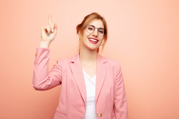 Young pretty blonde woman smiling cheerfully and happily, pointing upwards with one hand to copy space. business concept