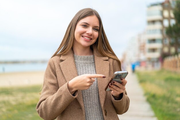 Young pretty blonde woman using mobile phone and pointing it
