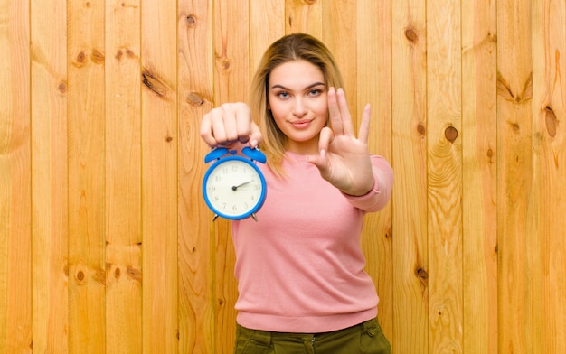 Young pretty blonde woman with an alarm clock against wood wall