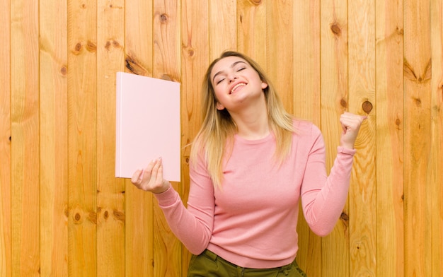 Giovane donna bionda graziosa con i libri contro la parete di legno