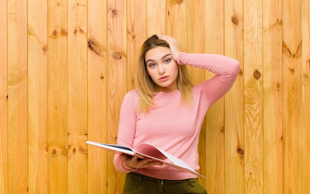 Young pretty blonde woman with books against wood 