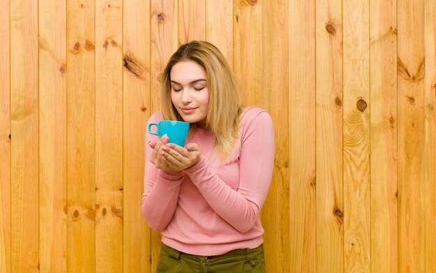 Young pretty blonde woman with a coffee cup against wood wall