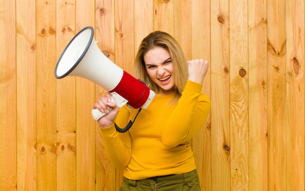 Photo young pretty blonde woman with a megaphone  wood wall