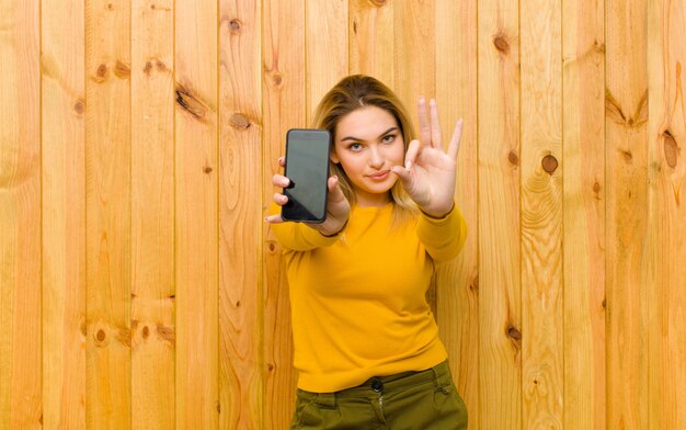 Giovane donna bionda graziosa con un telefono cellulare contro la parete di legno