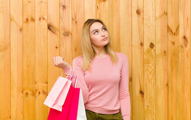Young pretty blonde woman with shopping bags against wood 