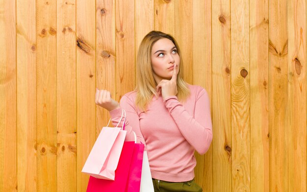 Young pretty blonde woman with shopping bags against wood 