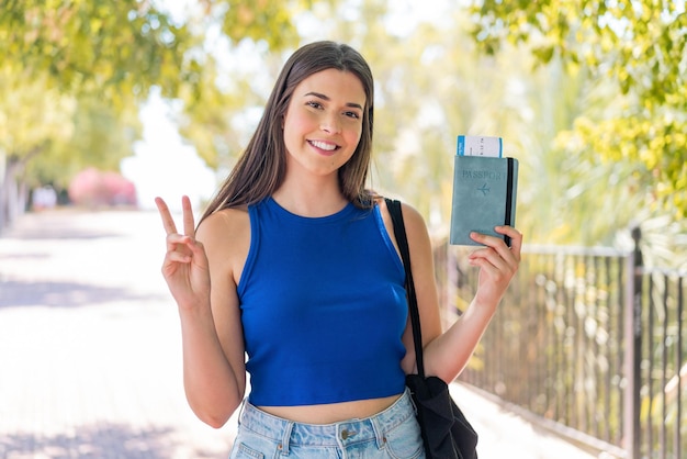 Young pretty Brazilian woman holding a passport at outdoors smiling and showing victory sign
