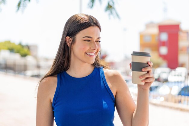 Young pretty Brazilian woman holding a take away coffee at outdoors with happy expression