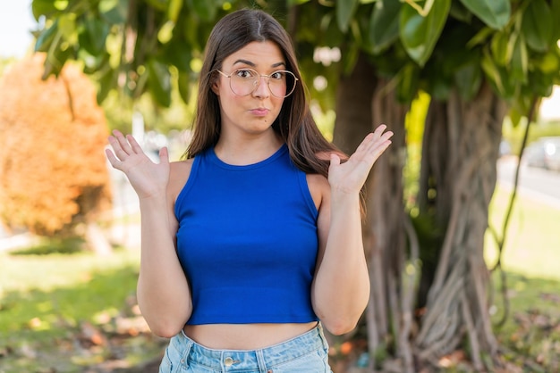 Photo young pretty brazilian woman with glasses at outdoors making doubts gesture