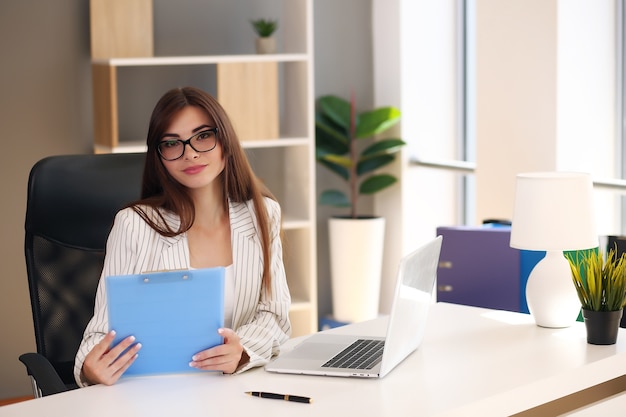 Young pretty brunette business woman with laptop in the office.