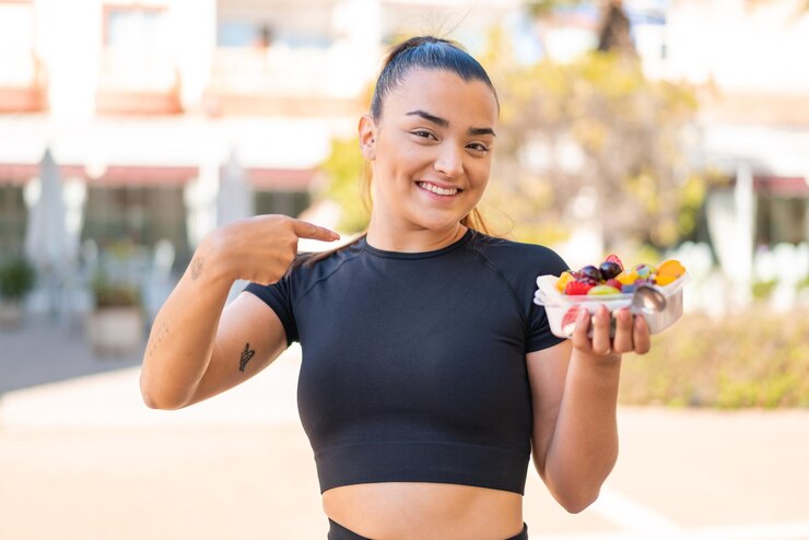 Young pretty brunette woman holding a bowl of fruit at outdoors with surprise facial expression