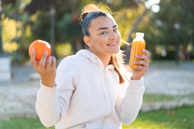 Young pretty brunette woman holding an orange and an orange juice