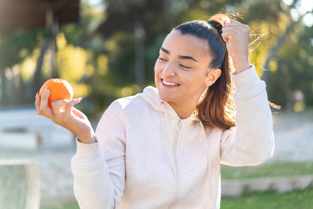屋外で勝利を祝うオレンジを保持している若いかなりブルネットの女性