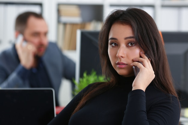 Young pretty brunette woman in office work with her boss hold phone in hands