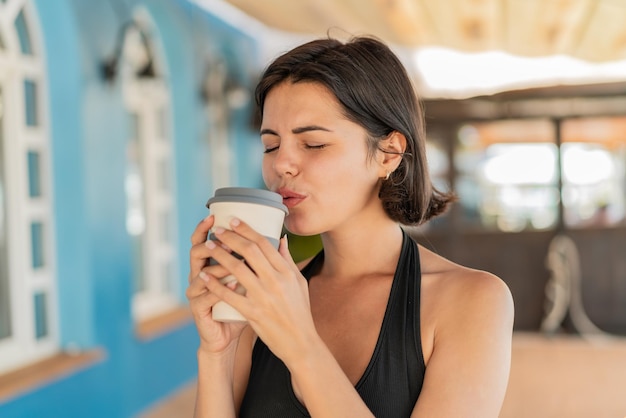 屋外でテイクアウトのコーヒーを持っている若いかなりブルガリア人女性