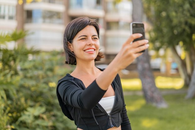야외에서 휴대전화로 셀카를 찍고 있는 젊고 예쁜 불가리아 여성