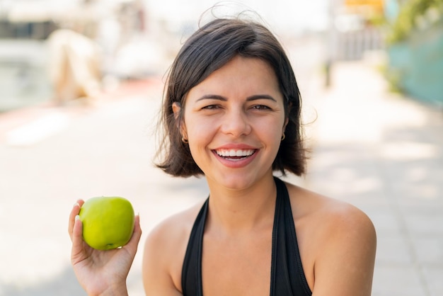 Young pretty Bulgarian woman at outdoors with an apple and happy