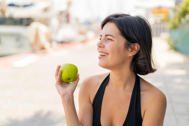 Photo young pretty bulgarian woman at outdoors with an apple and happy