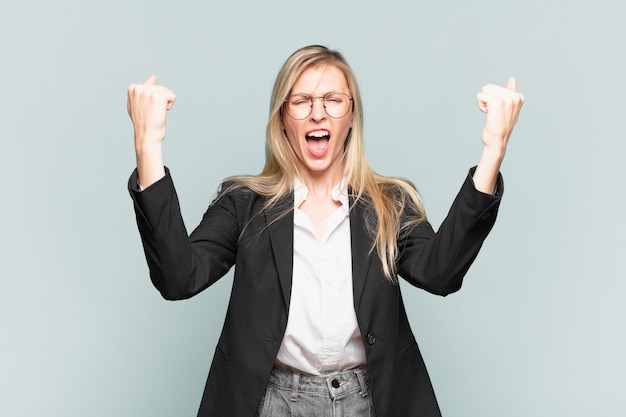 Young pretty businesswoman celebrating an unbelievable success like a winner, looking excited and happy saying take that!