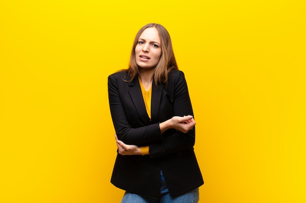 Young pretty businesswoman feeling anxious, ill, sick and unhappy, suffering a painful stomach ache or flu against orange wall