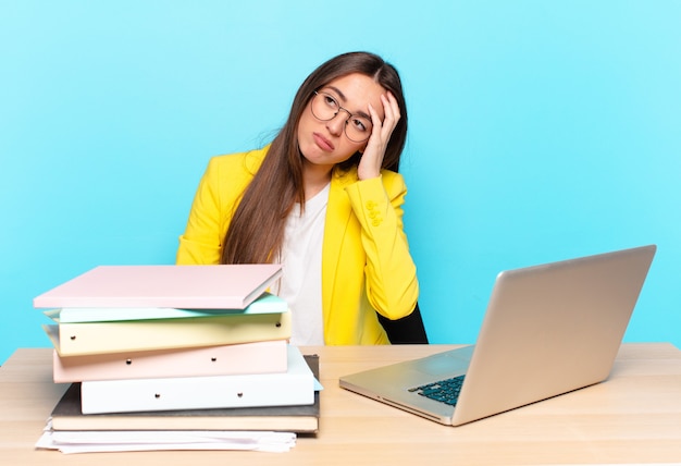 Young pretty businesswoman feeling bored, frustrated and sleepy after a tiresome, dull and tedious task, holding face with hand