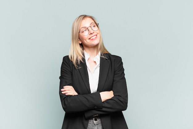 Young pretty businesswoman feeling happy, proud and hopeful, wondering or thinking, looking up to copy space with crossed arms