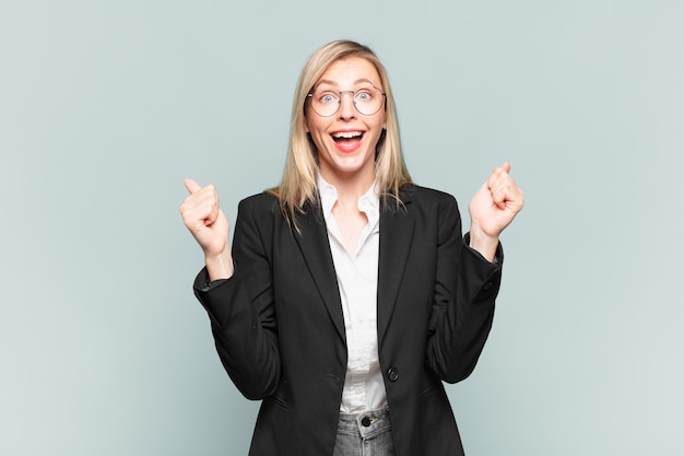 Young pretty businesswoman feeling shocked, excited and happy, laughing and celebrating success, saying wow!