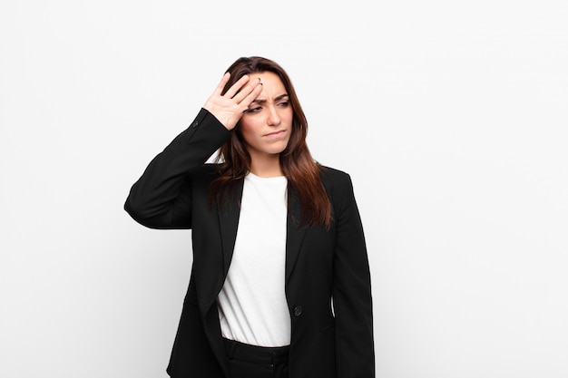 Young pretty businesswoman looking stressed, tired and frustrated, drying sweat off forehead, feeling hopeless and exhausted against white wall