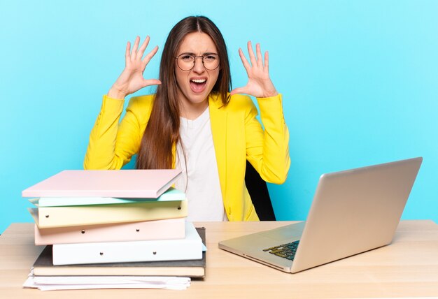 Young pretty businesswoman screaming in panic or anger, shocked, terrified or furious, with hands next to head