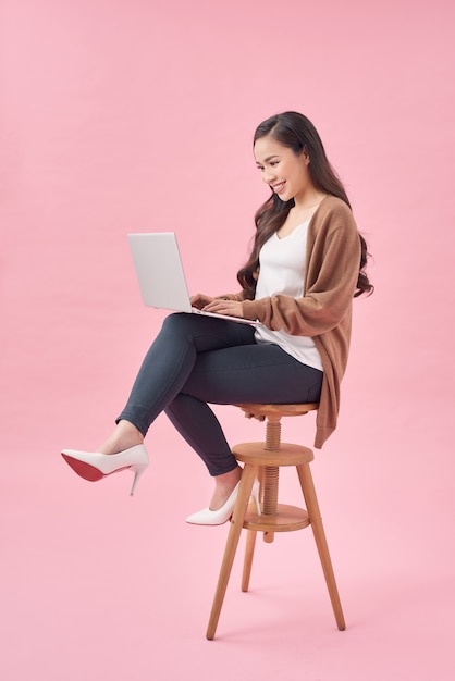 Young pretty businesswoman sitting on chair and typing on laptop