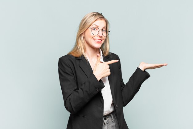 Young pretty businesswoman smiling cheerfully and pointing to copy space on palm on the side, showing or advertising an object