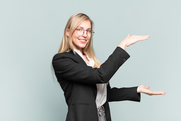 Young pretty businesswoman smiling, feeling happy, positive and satisfied, holding or showing object or concept on copy space