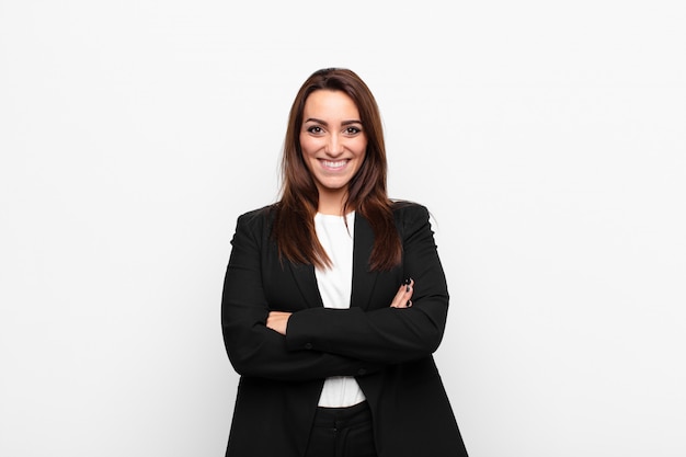 Young pretty businesswoman smiling with crossed arms and a happy, confident, satisfied expression, lateral view against white wall