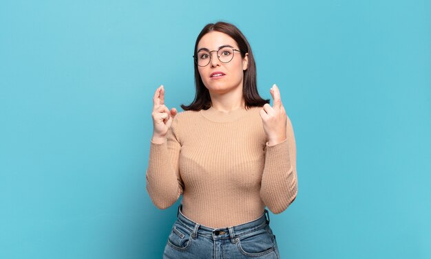 Young pretty casual woman crossing fingers anxiously and hoping for good luck with a worried look