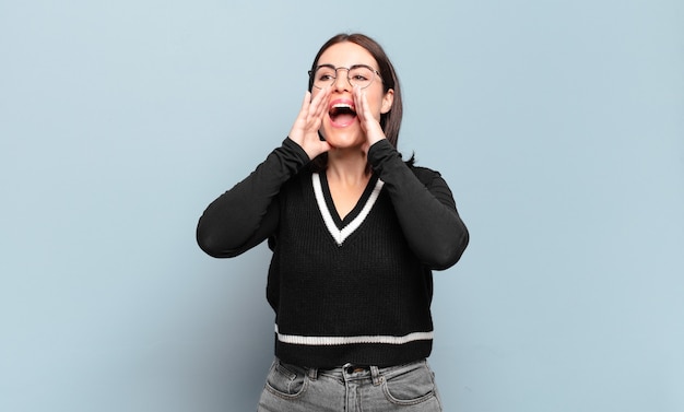 Young pretty casual woman feeling happy, excited and positive, giving a big shout out with hands next to mouth, calling out