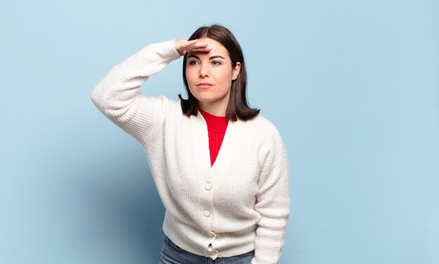 Young pretty casual woman looking bewildered and astonished, with hand over forehead looking far away, watching or searching