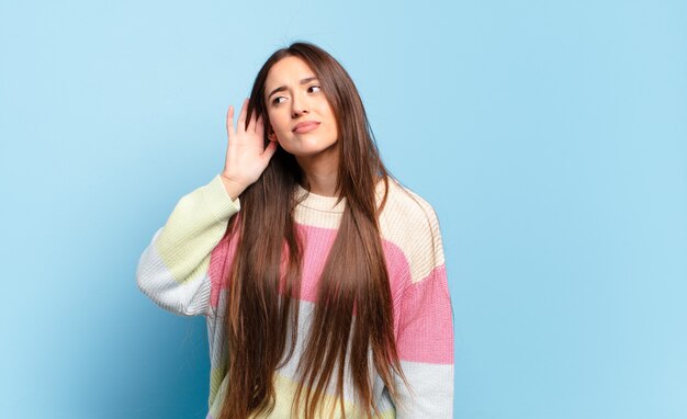 Young pretty casual woman looking serious and curious, listening, trying to hear a secret conversation or gossip, eavesdropping