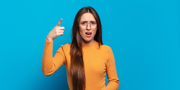 Young pretty casual woman pointing at camera with an angry aggressive expression looking like a furious, crazy boss