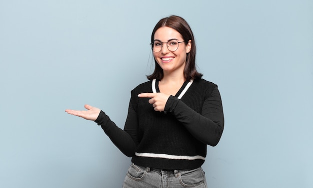 Young pretty casual woman smiling, feeling happy, carefree and satisfied, pointing to concept or idea on copy space on the side