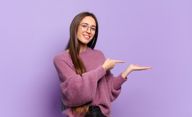 Young pretty casual woman smiling, feeling happy, carefree and satisfied, pointing to concept or idea on copy space on the side