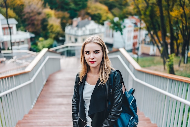 Young pretty casually dressed hipster girl tourist posing outdoors at the city park steps with a backpack