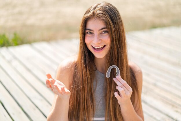 Young pretty caucasian woman holding invisible braces at outdoors with shocked facial expression