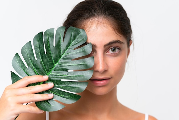 Photo young pretty caucasian woman isolated on white background holding a palm leaf close up portrait
