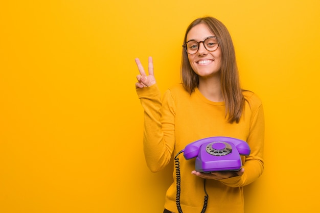 Giovane donna abbastanza caucasica che mostra il numero due. ha in mano un telefono vintage.